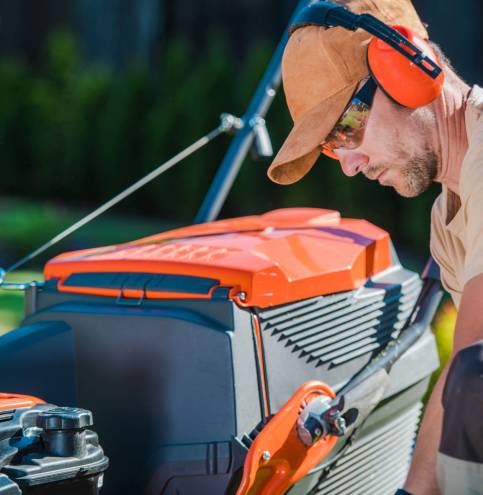 Professional Gardener Checking HIs Lawn Mower Before Starting th Male Caucasian Gardener focused on Inspecting His Equipment Before Starting Mowing the Lawn on His Client’s Backyard. Closeup of a Professional Garden Maintenance Service Worker.